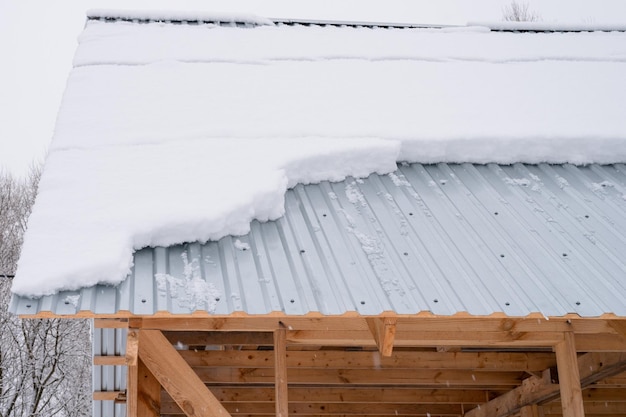 Neige glissant du toit bâtiment construction maison avec toit en métal recouvert de neige gelée fraîche et de flocons de neige le jour d'hiver glacial dans la banlieue du village de campagne saison d'hiver enneigée par temps froid