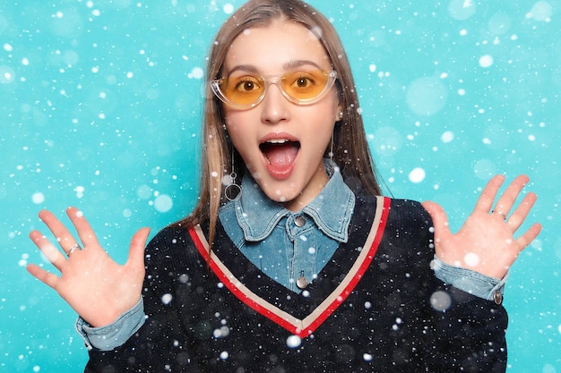 Neige, hiver, Noël, émotions, mode, personnes, jeunesse et concept de beauté - Gros plan d'une jeune femme élégante en lunettes de soleil souriant sur fond de neige. la fille est surprise