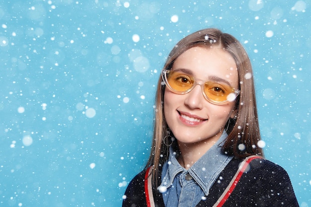 Neige, hiver, Noël, émotions, mode, personnes, jeunesse et concept de beauté - Gros plan d'une jeune femme élégante en lunettes de soleil souriant sur fond de neige