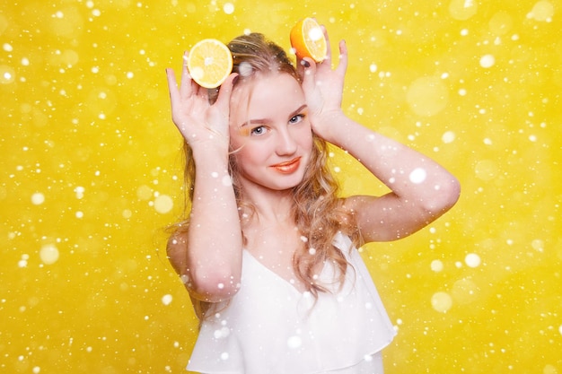 Neige, hiver, Noël, émotions, santé, personnes, nourriture et concept de beauté - Beauty Model Girl prend des oranges juteuses. Belle adolescente joyeuse avec des taches de rousseur. maquillage jaune. sur fond de neige