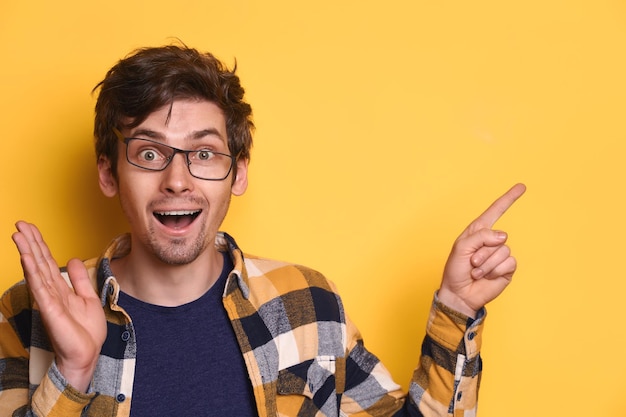 Un nerd drôle a l'air étonné et montre quelque chose sur le mur jaune du studio