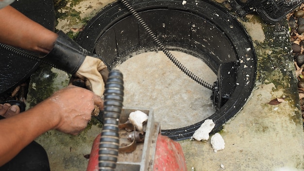 Nettoyage des canalisations. Plombier réparant le bac à graisse bouché avec la machine à vis. Entretien du système d'égout et du bac à graisse par un plombier professionnel. Utiliser un serpent à vis pour réparer et déboucher un drain.