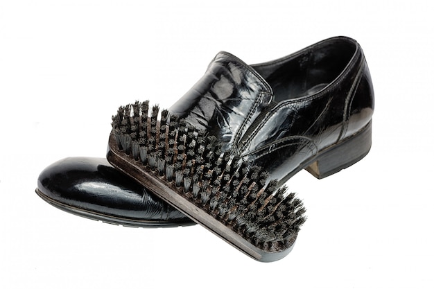 Nettoyage des chaussures ou des chaussures en prenant soin de concept, brosse en bois sur une chaussure noire nettoyée isolée sur blanc.