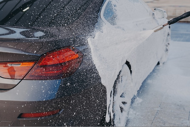 Nettoyage extérieur de voiture en appliquant de la mousse de neige sur une surface automobile sale à partir d'un nettoyeur haute pression