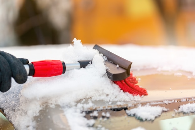 Nettoyage humain de la couverture neigeuse du toit de la voiture au soleil