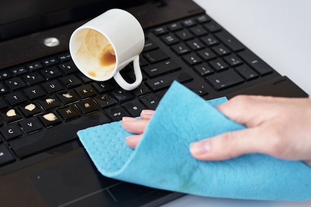 Nettoyage à la main du café renversé sur le clavier de l'ordinateur portable avec un chiffon
