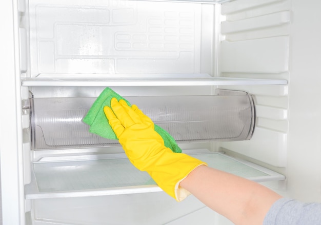 Nettoyage des mains du réfrigérateur Personne lavant le réfrigérateur avec un chiffon La femme de ménage essuie les étagères du réfrigérateur propre Main dans un gant de protection en caoutchouc jaune et une éponge verte lave