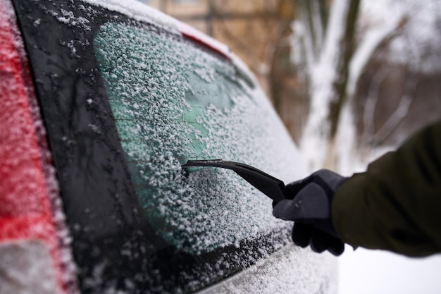 Nettoyage de la neige de la vitre arrière de la voiture avec un grattoir à glace avant le voyage L'homme enlève la glace de l'essuie-glace de la lunette arrière de la voiture