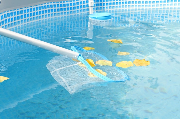 Le nettoyage d'une piscine avec un écumeur à maille Le long filet nettoie les feuilles colorées de la surface de l'eau