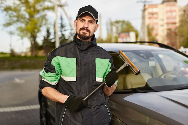 Nettoyant barbu avec éponge debout près de la voiture