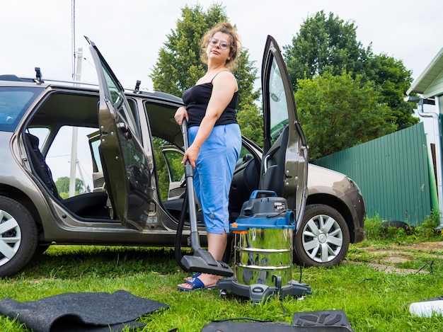 En nettoyant la voiture, la fille ramasse les miettes avec un aspirateur dans la voiture