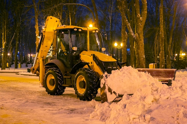 Nettoyer la neige dans le parc en hiver avec un tracteur le soir