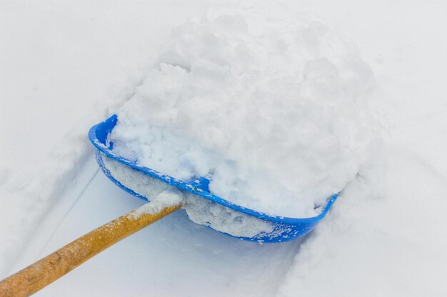 Nettoyer la neige fraîche avec une pelle en plastique bleue à l'extérieur en hiver