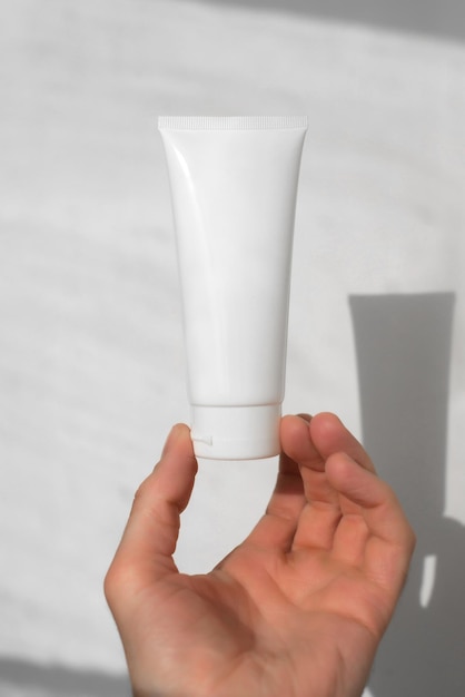 Nettoyer le tube blanc de crème hydratante sur fond blanc à la main