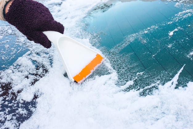 Nettoyer la vitre de la voiture de la glace avec un grattoir