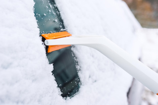 Nettoyer les vitres de la voiture de la neige avec un grattoir