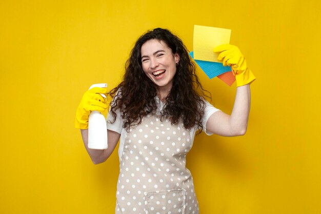 Le nettoyeur de fille en tablier contient des chiffons et un agent de nettoyage sur fond jaune