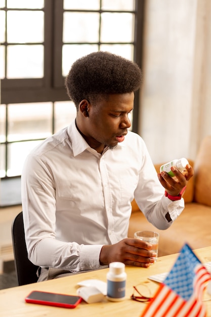 Nice bel homme regardant la bouteille avec des pilules tout en lisant à leur sujet