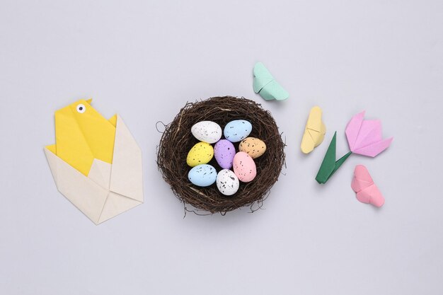 Nid avec des oeufs de caille colorés et des papillons de tulipes de poulet origami sur fond gris Composition de Pâques