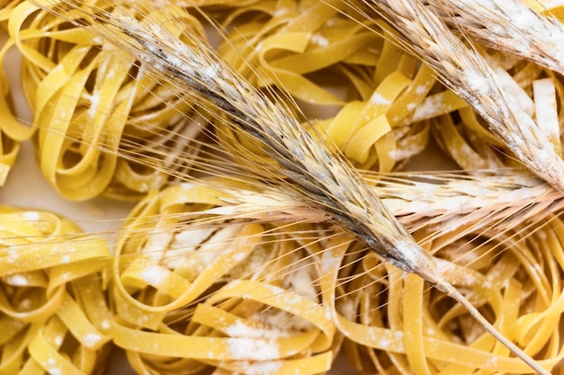 Nid de pâtes de blé dur saupoudré de farine sur un fond blanc gros plan d'épillets de blé cuisine maison fond de pâtes