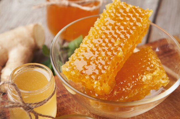 Nids d'abeilles frais dans un bol en verre et un pot de miel sur une table en bois, gros plan