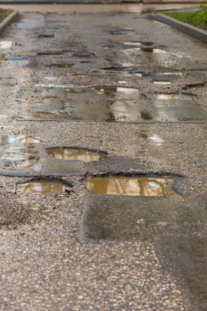 Nids-de-poule et flaques d'eau sur une mauvaise route goudronnée mouillée après la pluie