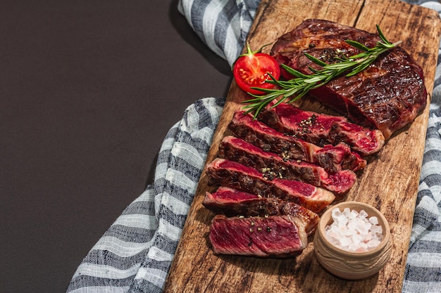Niveau de cuisson rare Bifteck de faux-filet aux épices et herbes Coupe de viande grillée classique prête à manger Concept de pique-nique ou de dîner Lumière dure ombre noire fond de pierre noire espace de copie plat