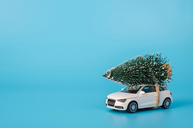 Noël arrive concept. Close up side photo of toy mini car avec petit arbre de Noël sur le dessus isolé sur fond bleu