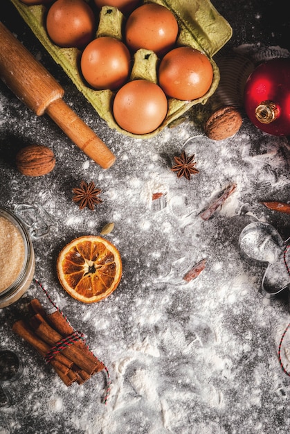 Noël, cuisine de vacances. Ingrédients, épices, oranges séchées et moules à pâtisserie, décorations de Noël (boules, branche de sapin, cônes), sur table en pierre noire,