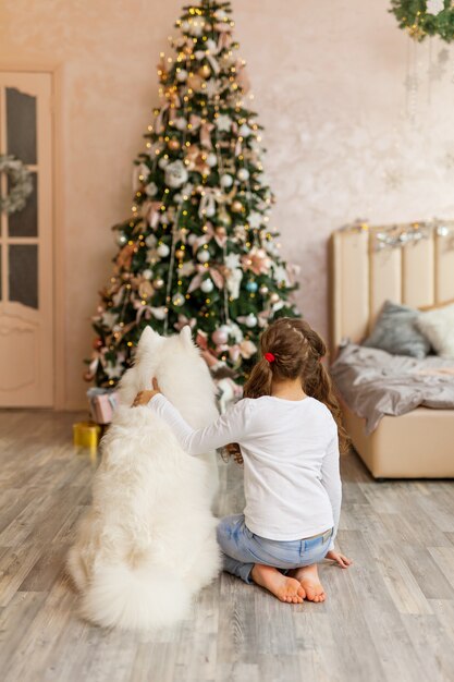 Noël enfant fille avec chien Samoyède devant un arbre de Noël