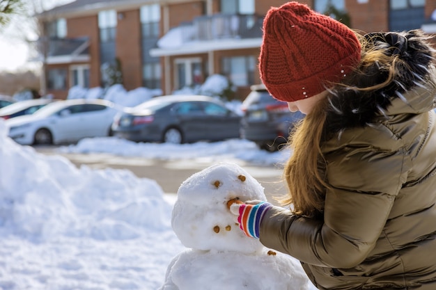 Noël enfant heureux sculpte un hiver de bonhomme de neige dans le parc la neige sur l'aire de jeux