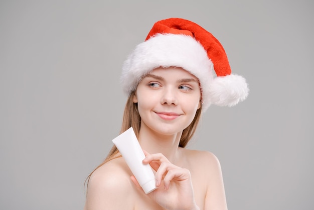 Noël femme modèle de beauté au chapeau du père Noël tient un tube blanc dans sa main