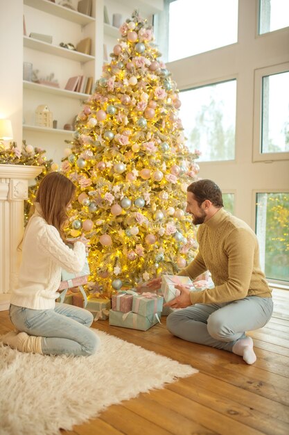 Noël. Jeune couple heureux assis près de l'arbre de Noël