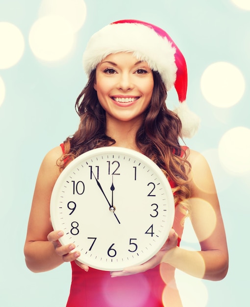 noël, noël, hiver, concept de bonheur - femme souriante en bonnet de noel avec horloge montrant 12