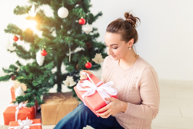 Noël, Noël, hiver, concept de bonheur - la fille ouvre un cadeau dans le contexte de l'arbre de Noël. Heureuse jeune femme célébrant Noël