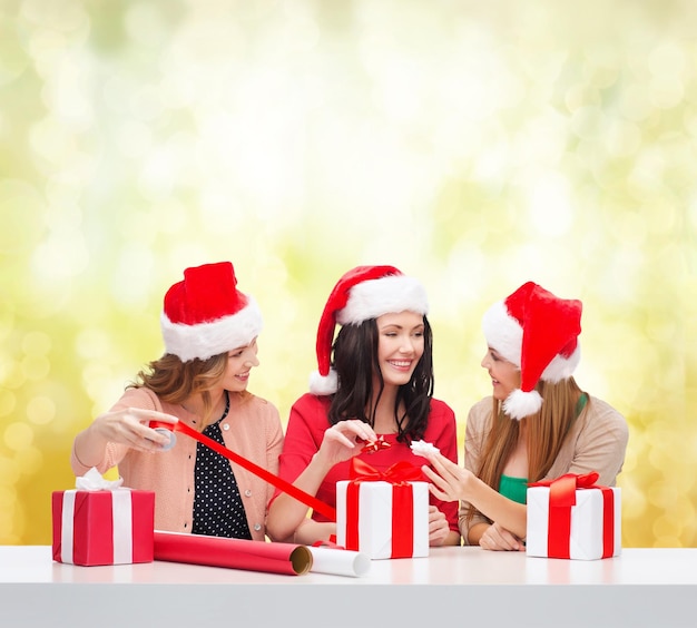 noël, noël, hiver, concept de bonheur - trois femmes souriantes dans des chapeaux d'aide de santa avec des coffrets cadeaux