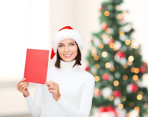 Noël, Noël, personnes, publicité, concept de vente - femme heureuse en bonnet de Noel avec carte rouge vierge