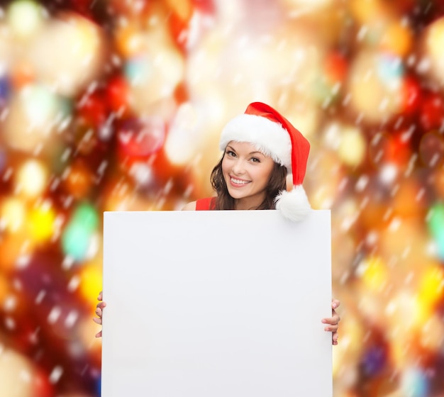 Photo noël, noël, personnes, publicité, concept de vente - femme heureuse en bonnet de noel avec tableau blanc vierge