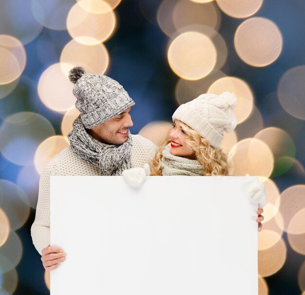 Noël, Noël, personnes, publicité, couple, concept de vente - femme et homme heureux en vêtements d'hiver avec tableau blanc vierge