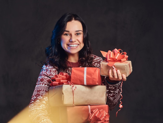 Noël, Saint Valentin, Nouvel an. Portrait d'une fille brune heureuse portant un chandail chaud tenant une boîte-cadeau, isolée sur un fond texturé sombre.