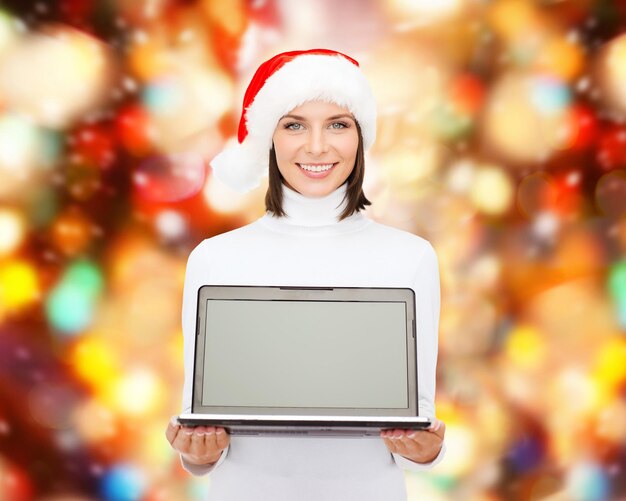 Photo noël, technologie, vacances d'hiver et concept de personnes - femme souriante en bonnet d'assistance avec ordinateur portable à écran blanc sur fond de feux rouges