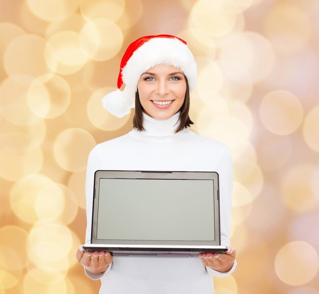 Noël, technologie, vacances d'hiver et concept de personnes - femme souriante en bonnet d'assistance avec ordinateur portable à écran blanc sur fond de lumières beiges