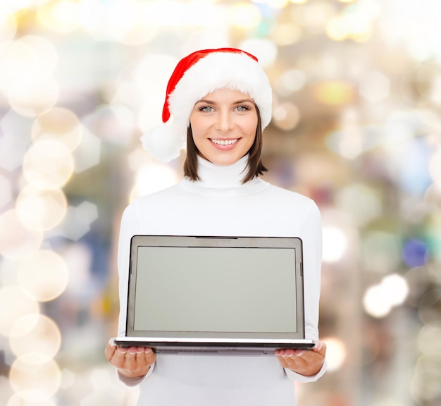 Noël, technologie, vacances d'hiver et concept de personnes - femme souriante en bonnet d'assistance avec ordinateur portable à écran blanc sur fond de lumières