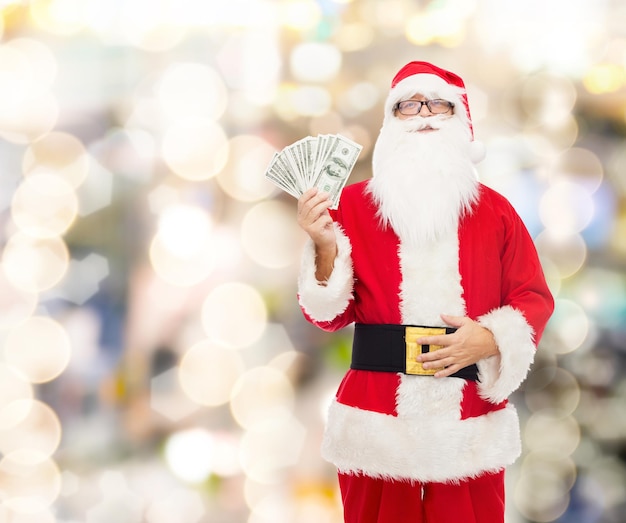 noël, vacances, gagner, monnaie et concept de personnes - homme en costume de père noël avec de l'argent en dollars sur fond de lumières