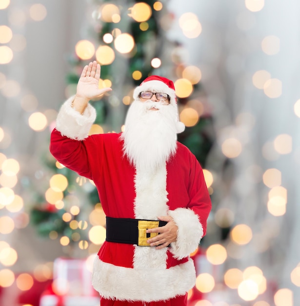 noël, vacances, geste et concept de personnes - homme en costume de père noël agitant la main sur fond de lumières d'arbre