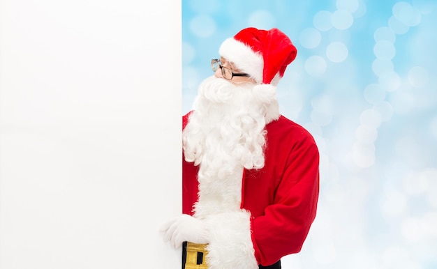 noël, vacances, publicité et concept de personnes - homme en costume de père noël avec panneau d'affichage blanc vierge sur fond de lumières bleues