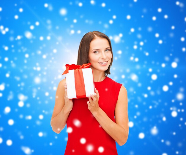 Photo noël, vacances, saint valentin, célébration et concept de personnes - femme souriante en robe rouge avec boîte-cadeau sur fond bleu neigeux