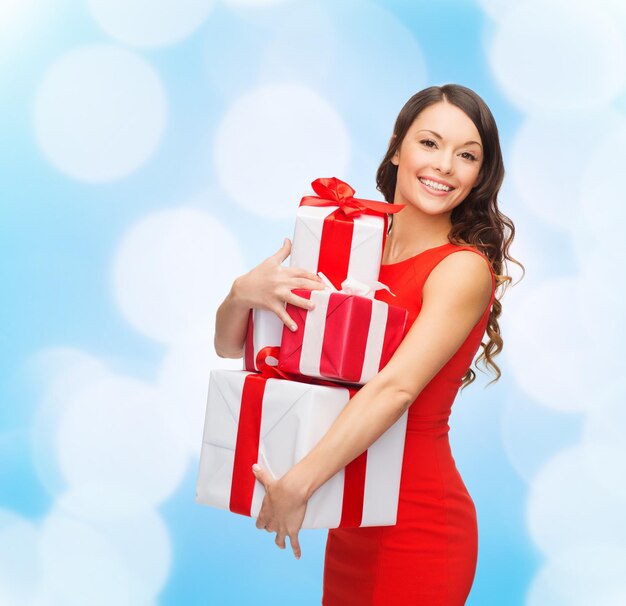 noël, vacances, saint valentin, célébration et concept de personnes - femme souriante en robe rouge avec des coffrets cadeaux sur fond de lumières bleues