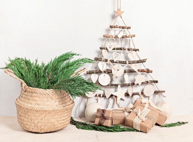 Photo noël zéro déchet avec des cadeaux emballés dans du papier kraft et un arbre de noël fait main alternatif suspendu au mur léger