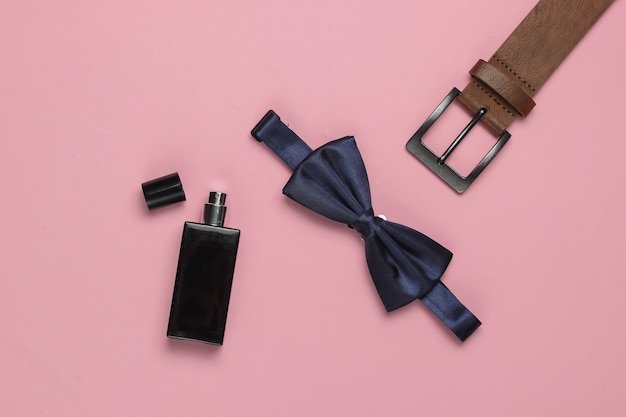 Noeud papillon, ceinture, flacon de parfum sur fond rose. Accessoires pour hommes. Style formel, préparation du mariage.